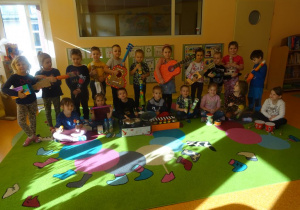 Grupa dzieci stoi lub siedzi wspólnie i pozują z instrumentami muzycznymi wykonanymi z materiałów pochodzących z recyklingu.
